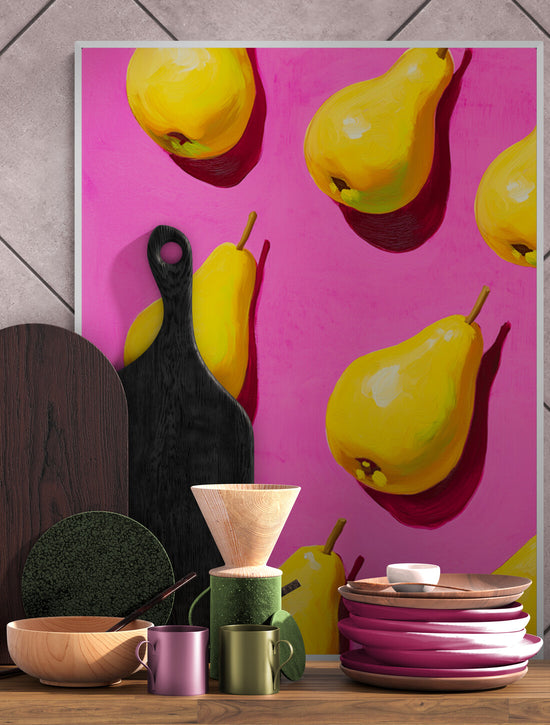 Affiche encadrée avec un design pop-art de poires jaunes sur un fond rose, placée contre un mur en carrelage. Entourée d’ustensiles et de vaisselle en bois, vert et rose, elle crée une ambiance chaleureuse et artistique, idéale pour une cuisine tendance.