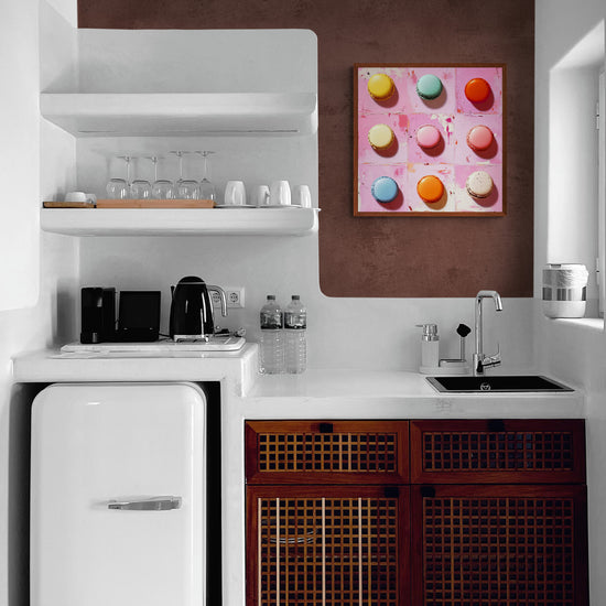 Une cuisine au design rétro avec un mur texturé brun. Des meubles en bois tressé foncé rappellent un style ancien, tandis que des étagères blanches épurées modernisent l’ensemble. Un tableau aux tons rose et pastel, représentant des macarons, illumine l’espace au-dessus du plan de travail.