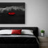 Une impression murale du bateau rouge flottant sur une mer noire est accrochée au-dessus d’un lit minimaliste avec des draps noirs et un coussin rouge assorti au tableau.