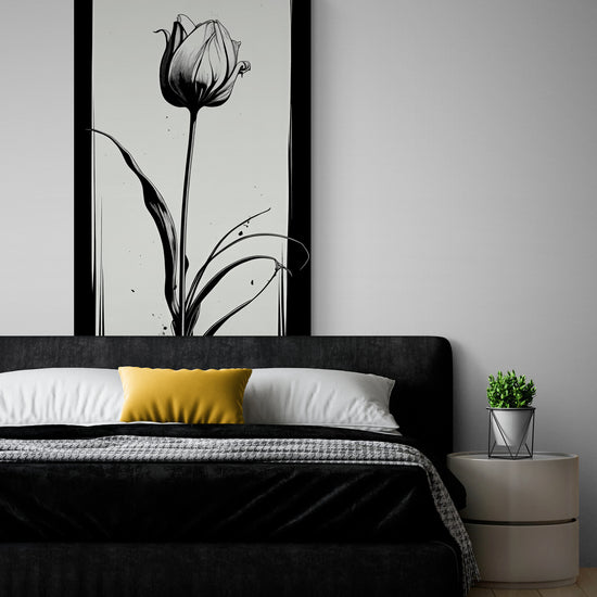 Dans une chambre au style épuré et contemporain, une grande toile représentant une tulipe en noir et blanc est accrochée au-dessus du lit. La pièce est décorée dans des tons neutres, avec une tête de lit sombre contrastant avec le linge de lit blanc et gris. Un coussin jaune apporte une touche de chaleur