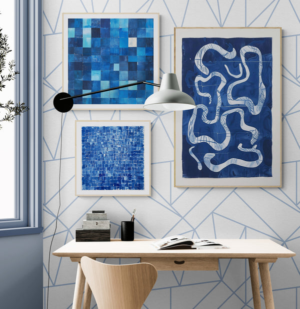 Un bureau moderne et épuré avec un mur géométrique blanc et bleu. Trois tableaux abstraits aux nuances de bleu décorent l’espace, apportant une touche artistique. Une lampe murale au design industriel éclaire le bureau en bois clair, accompagné d’une chaise assortie. Une fenêtre laisse entrer la lumière naturelle, renforçant l’ambiance apaisante