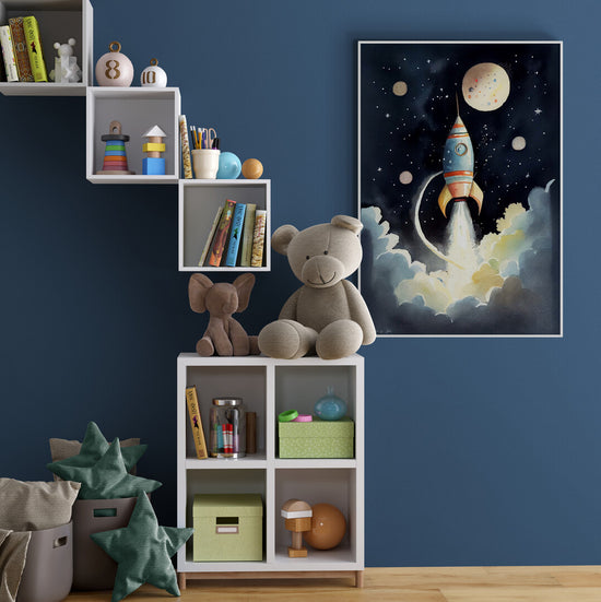 Une chambre d’enfant bien organisée, avec des étagères blanches en escalier, remplies de livres et de jouets en bois. Un grand ours en peluche est assis sur un des casiers. Sur le mur bleu, un tableau représentant une fusée en plein décollage ajoute une touche d’imaginaire.