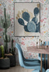 Tableau cactus stylisé Papier peint floral Cactus en pot Chaises modernes bleu clair Table en bois et métal doré Bougeoirs dorés Sol en bois clair Éclairage naturel Style éclectique et moderne Ambiance botanique