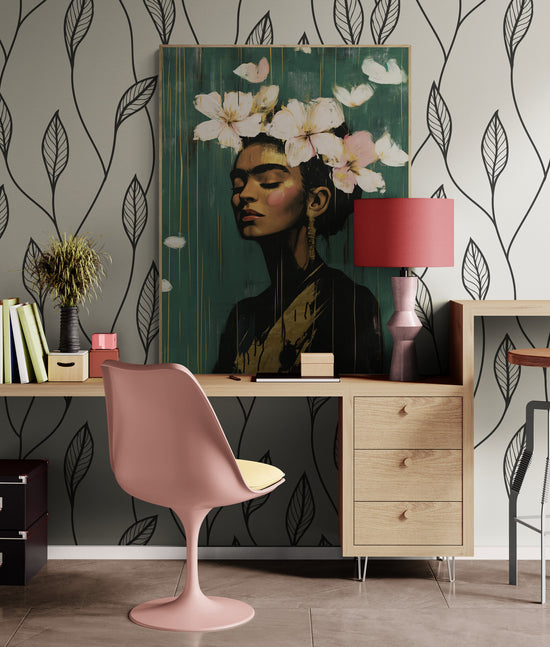 ableau de Frida Kahlo accroché au mur d'un bureau moderne avec une chaise rose et un bureau en bois clair. Le décor est rehaussé par un papier peint à motifs de feuilles noirs sur fond gris