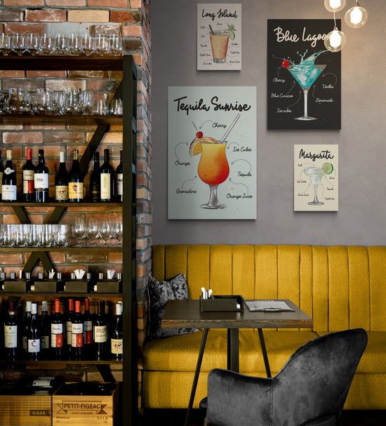 Un restaurant avec sur la droite une étagère pleine de bouteilles de vin et sur la gauche au-dessus d’une banquette en daim jaune, une décoration avec plusieurs tableaux de la même collection accroché au mur . Sur chaque toile un verre de cocktail différent et les ingrédients nécessaires à sa réalisation