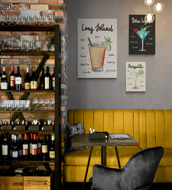 Un restaurant avec sur la droite une étagère pleine de bouteilles de vin et sur la gauche au-dessus d’une banquette en daim jaune, une décoration avec plusieurs tableaux de la même collection accroché au mur . Sur chaque toile un verre de cocktail différent et les ingrédients nécessaires à sa réalisation