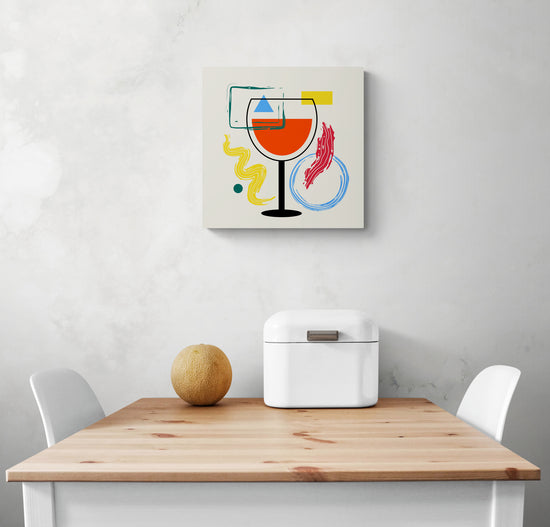 Tableau déco cuisine moderne est accroché au centre d'un mur blanc. Le tableau minimaliste sur la toile au centre une l'illustration d'un verre de vin noir. Autour du verre des formes géométriques carré, rectangle, triangle et rond et des formes aux pinceaux. En dessous une table de repas blanche, et a chaque extrémité une chaise blanche. Un melon et une boîte à pain blanc sont sur la table.