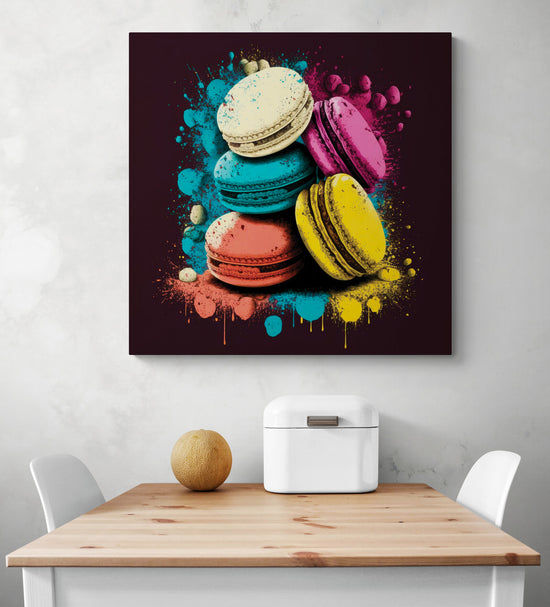 Un tableau cuisine macaron multicolore sur fond noir dans un style pop art des éclaboussures de peinture. Ce tableau cuisine est placé ce au-dessus d'une table en bois et deux chaises sont de chaque côté.