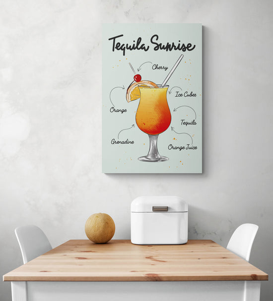 Dans une cuisine, sur un mur blanc avec des nuances de gris il y a une toile murale. Sur le tableau en fond bleu une illustration d’un verre de cocktail tequila sunrise avec les ingrédients écrit avec une police d’ecriture manuscrite. Au-dessous du cadre, une table de repas en bois et deux chaises blanches. Une corbeille à pain en métal blanc et un melon sont sur le dessus de la table.